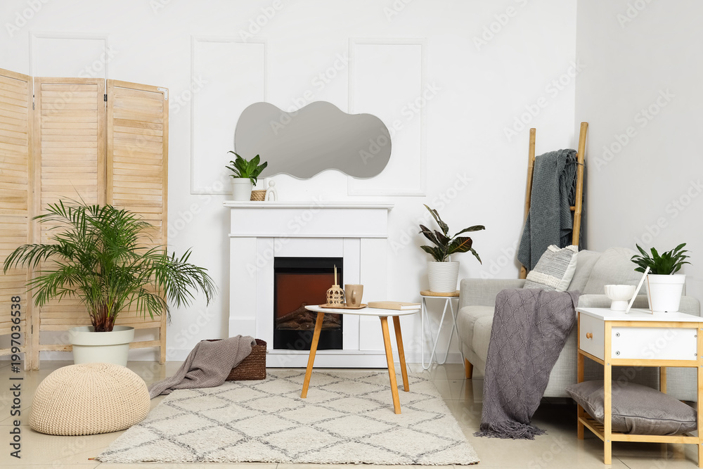 Naklejka premium Interior of light living room with mirror, grey sofa and fireplace