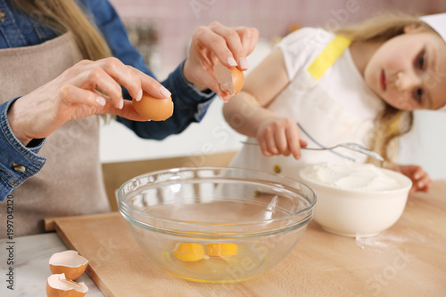 Photography Mother and her daughter cooking together at white table in kitchen, closeup