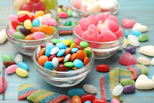 Foto Delicious colorful candies in glass bowls on blue wooden table, closeup