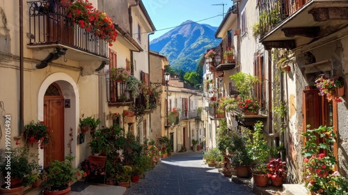 Charming Italian Village Street Lined With Flower-Adorned Buildings and Potted Plants Leading to a Majestic Mountain Vista Under a Clear Blue Sky