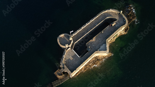 Aerial view of the imposing Chateau du Taureau, a stone fortress rising from the dark waters, its weathered walls catching the golden light, Plouezoc'h, Bretagne, France.