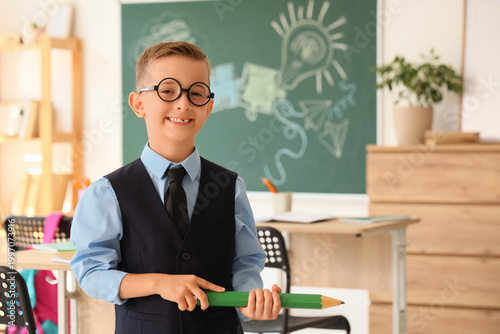 Cute little schoolboy with large pencil in classroom