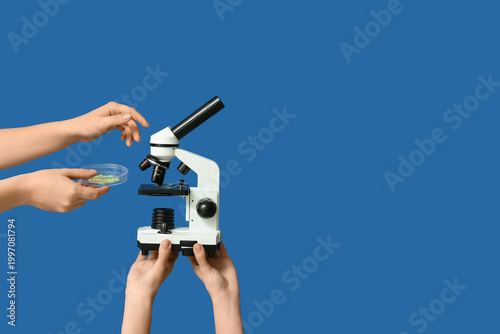 Female hands with modern microscope and Petri dish of sample on blue background