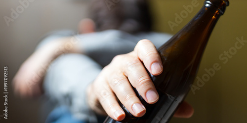Fotografie Extended arm and hand holding beer bottle in closeup panoramic crop for alcohol