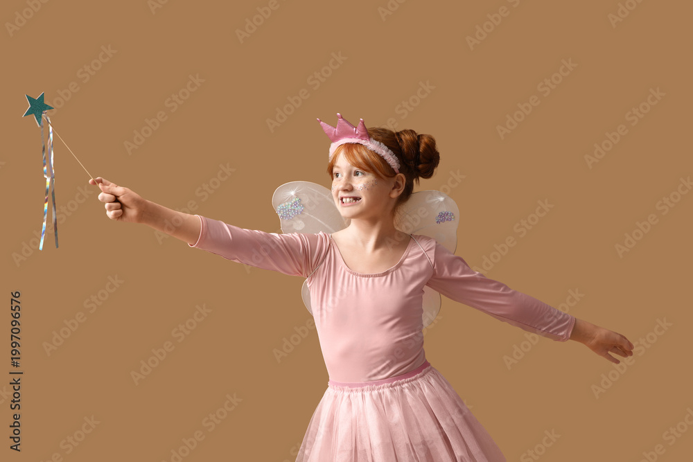 Fototapeta premium Cute girl in fairy costume playing with magic wand on brown background