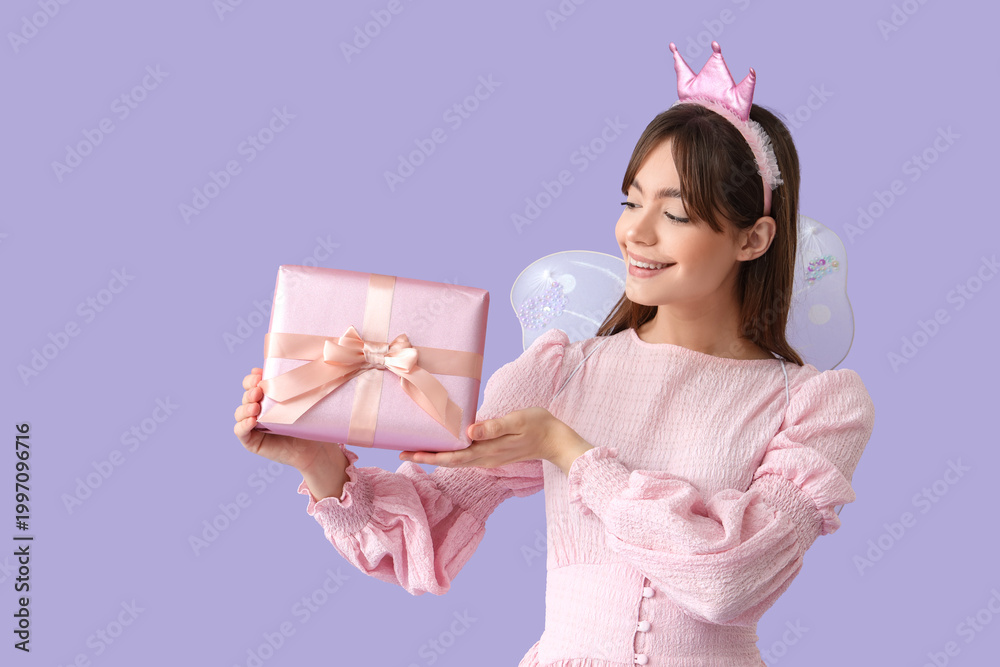 Fototapeta premium Young woman in fairy costume with gift box on lilac background