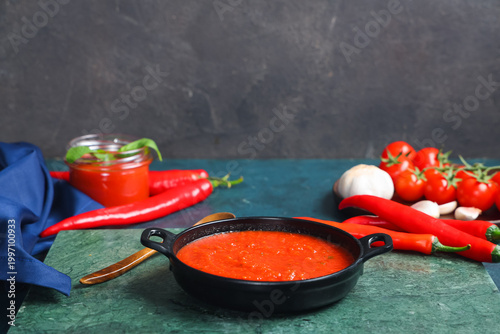 Foto Frying pan of tomato sauce with chili peppers and garlic on dark table