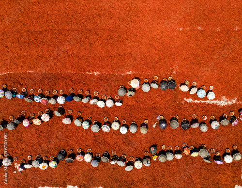 Aerial view of a vibrant tapestry of individuals gathered in solemn unity on an earthy red expanse, Sariakandi, Rajshahi Division, Bangladesh.