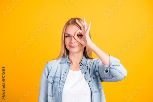 Quadro su tela Young woman making an OK gesture around her eye while smiling against a vibrant