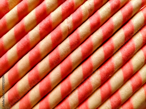 Diagonal arrangement of wafer roll cookies with a spiral pattern. Each stick alternates between beige and red stripes, creating a visually appealing contrast.