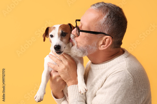 Senior man kissing cute dog on yellow background