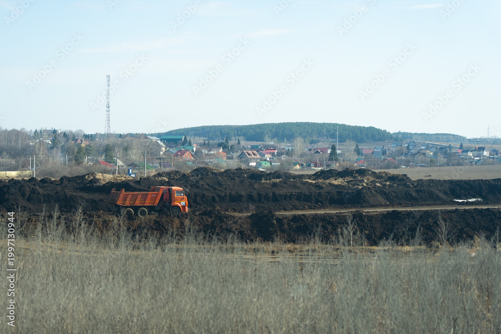 Fototapeta premium Construction Site with an Orange Dump Truck Working on Earth Moving and Land Preparation for Future Development in a Rural Landscape