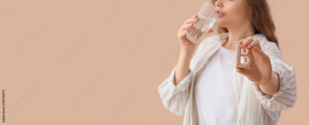 Obraz premium Young woman taking vitamin B on beige background with space for text