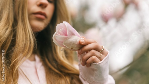 Bilde på lerret Young woman gently holding a delicate pink magnolia flower in her hand