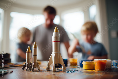 Family time spent building a small rocket model while children enjoy painting together in a cozy indoor setting