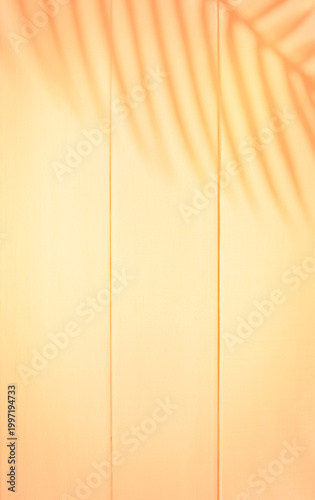 Warm minimal background with soft sunlight casting tropical palm leaf shadows on a light beige wooden surface. Natural texture with vertical lines and warm tones creates a cozy, summer, and lifestyle 