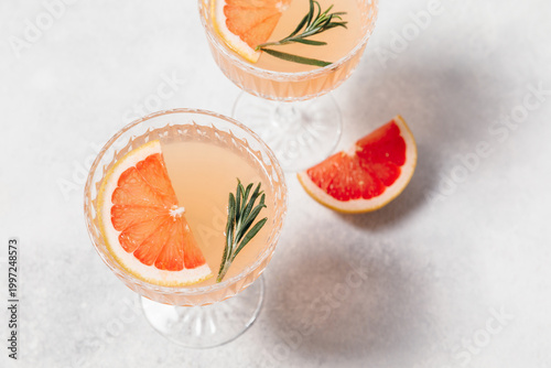 Elegant grapefruit and rosemary cocktails served in crystal glasses with fresh grapefruit slices, set against a light background. Perfect for summer gatherings and holiday party. Refreshing mocktail.