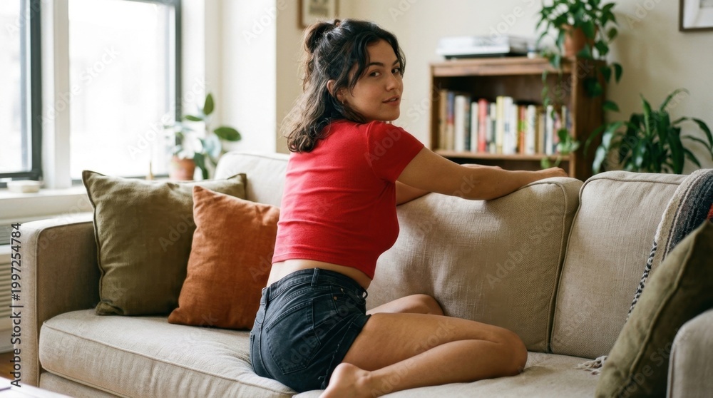 Fototapeta premium Young woman relaxing on a cozy sofa at home, casually turning to look back at the camera.