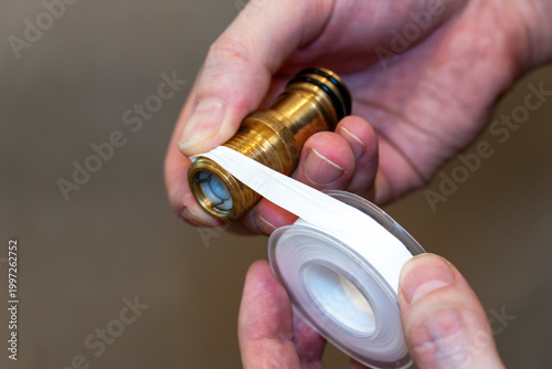Hands wrapping thread seal tape around brass plumbing fitting, leak prevention DIY repair concept.