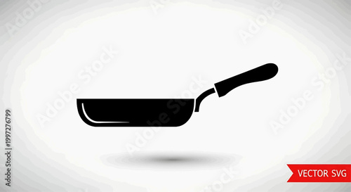 A frying pan sits on a surface with its handle pointing right.