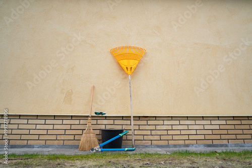 yellow rake, garden pruners and bucket by the wall of the house, garden tools