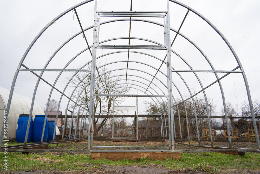 Naklejka premium Metal frame of a greenhouse in a private garden, land plot in spring