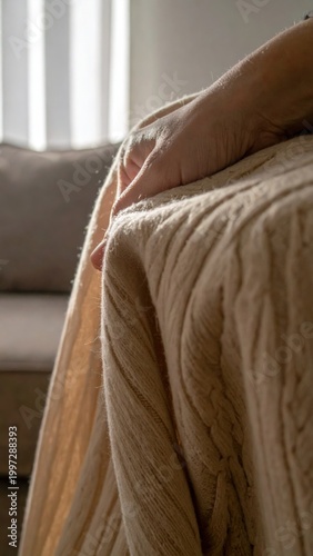 Elderly person hand resting on a soft beige knitted wool blanket in a cozy room, warmth, relaxation, comfort, peaceful indoor atmosphere, winter lifestyle