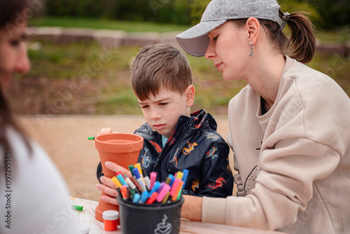 Boy and mother sitting at table decorating terracotta pots with colorful markers