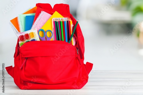 Red Backpack Filled With School Supplies on a Table in a Classroom Setting