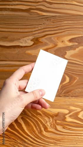 Hand holding blank white paper card template against a rustic textured wood grain background, ideal for business branding, promotion, or invitations