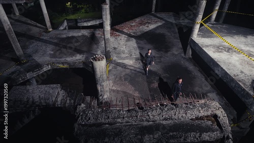 A high-angle shot shows a group of people walking away and disappearing down a staircase in a dark, abandoned concrete building, creating a sense of finality and mystery.