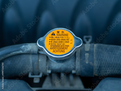 Macro close-up of an automobile radiator cap with warning text on the engine coolant system. Concept of car maintenance, overheating prevention, automotive repair, and vehicle safety inspection