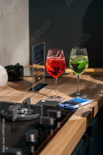 Two colorful cocktails on a modern kitchen counter beside a smartphone and stovetop, creating a stylish, relaxed lifestyle scene with warm light and contemporary design.