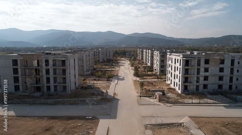 Aerial view of an uncompleted residential development surrounded by mountains, showcasing modern architecture and open spaces.