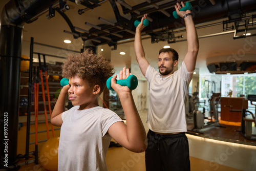 Adult man and boy lifting teal dumbbells in gym