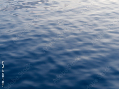 Abstract blue water surface texture with gentle ripples and soft sky reflections on the calm Mediterranean Sea.