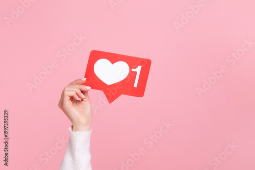 Hand holding red social media like notification icon for online popularity or marketing isolated over pink background with copy space