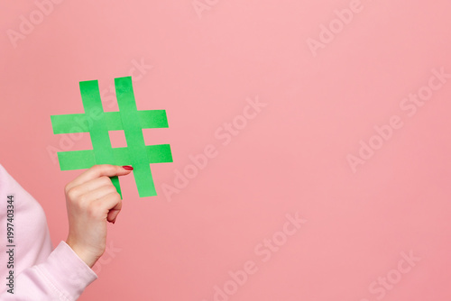 Cropped closeup view of anonymous woman's hands holding trending hashtag digital symbol online management system viral tracking tag isolated on pink background with copy space