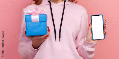 Cropped closeup view of faceless woman holding present box and smartphone with empty screen digital device with area for advertisement on display isolated on pink background