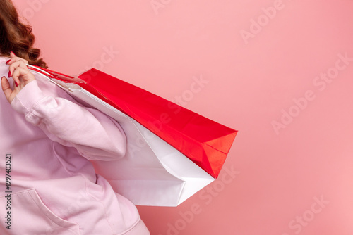 Cropped closeup view of unrecognizable woman holding shopping bags retail purchase sale store discount marketing commercial fashion weekend isolated on pink background with copy space