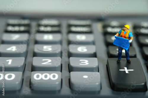 Miniature people toy figure photography. Project budget cost calculation concept. A construction worker with blueprint building standing above calculator. Isolated on white background