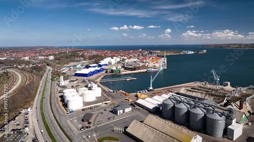 Aerial footage of coastal industrial port with storage tanks, silos, warehouses, container and shipping infrastructure. Industrial port, marina and coastal cityscape of Fredericia, Denmark.