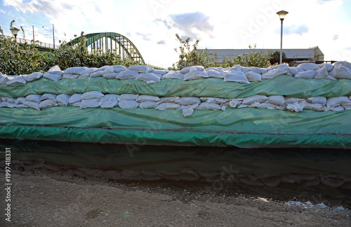 Wall of Sandbags and Tarp Plastic for Floods Protection Near River Arch Bridge