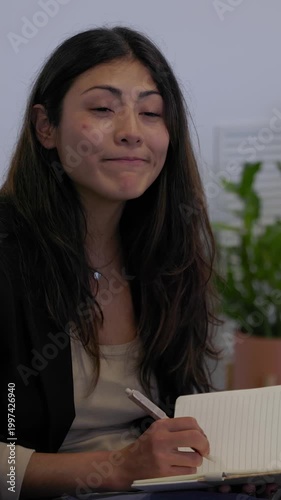 Vertical HD video of Latin American woman taking notes during informal team meeting in office. Young professional collaborating with coworkers while seated in a discussion circle