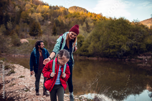 Parents and child hiking along forest lake trail in the mountains