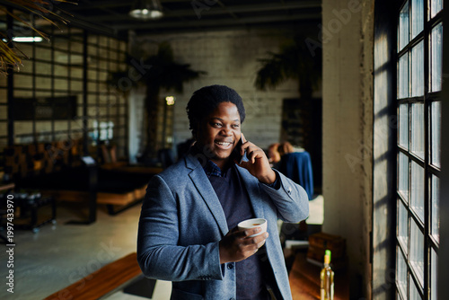Smiling businessman talking on smartphone by cafe window with coffee