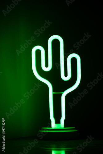 Green neon cactus lamp glowing in dark background.