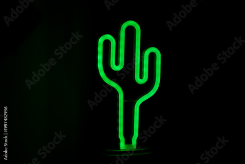 Green neon cactus lamp glowing in dark background.