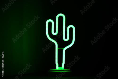 Green neon cactus lamp glowing in dark background.