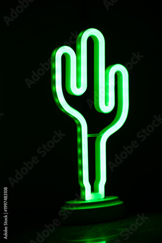 Green neon cactus lamp glowing in dark background.